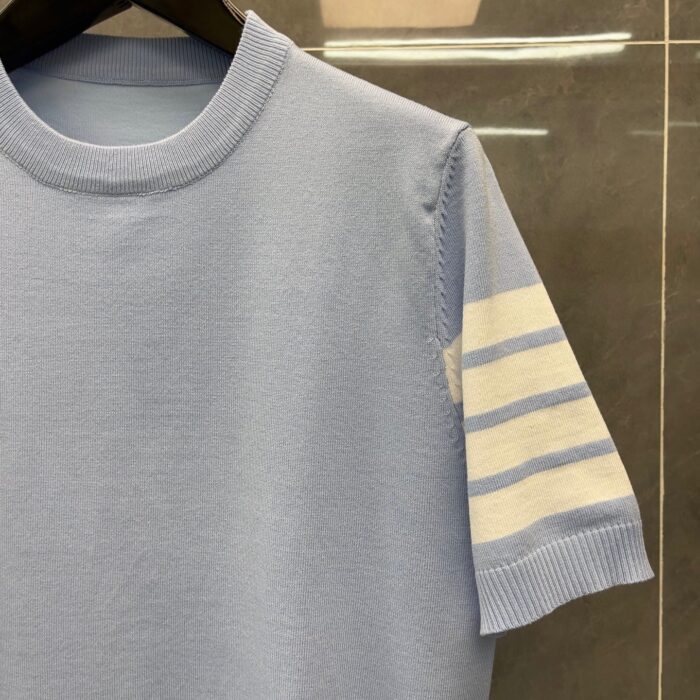 Maglietta blu chiaro con manica a righe crema, stile vintage e design elegante.