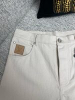 Pantaloni chiari in denim con logo in pelle, stile chic e versatile per ogni look.
