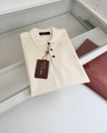Camicia polo crema in esposizione, elegante e versatile, con dettaglio ricamato e etichetta in vista.