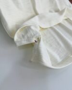 Dettaglio di camicia in lino crema con cuciture precise e piccolo dettaglio rosso.