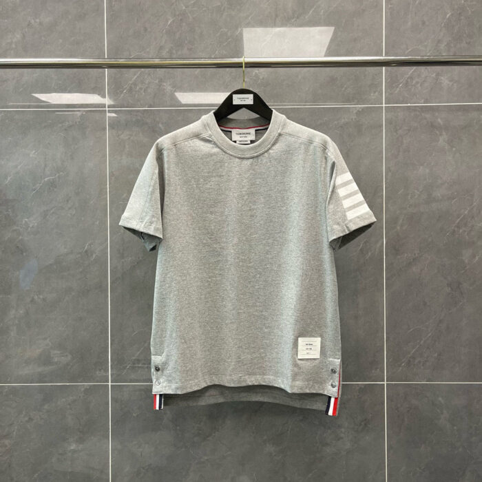 T-shirt grigia casual con strisce sportive sul braccio e etichetta minimal sul fondo.