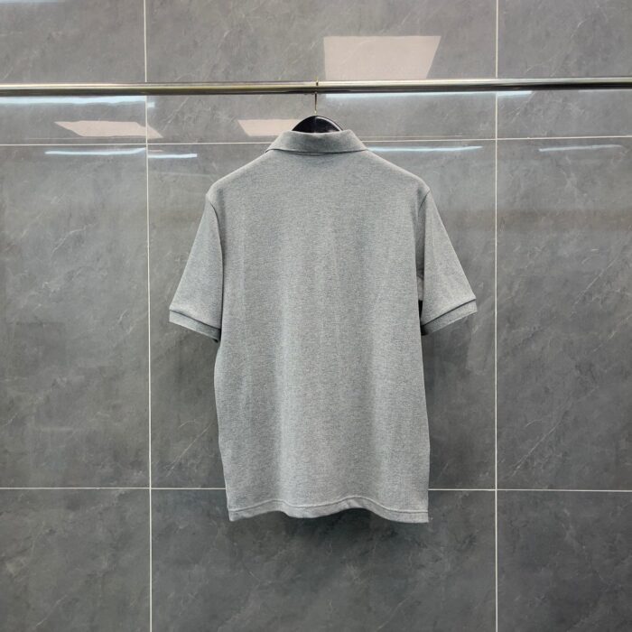 Maglietta polo grigia elegante su vetrina moderna, tessuto morbido e stile casual raffinato.