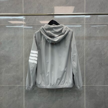 Giacca sportiva grigia con cappuccio e strisce bianche sulla manica, stile casual e moderno.