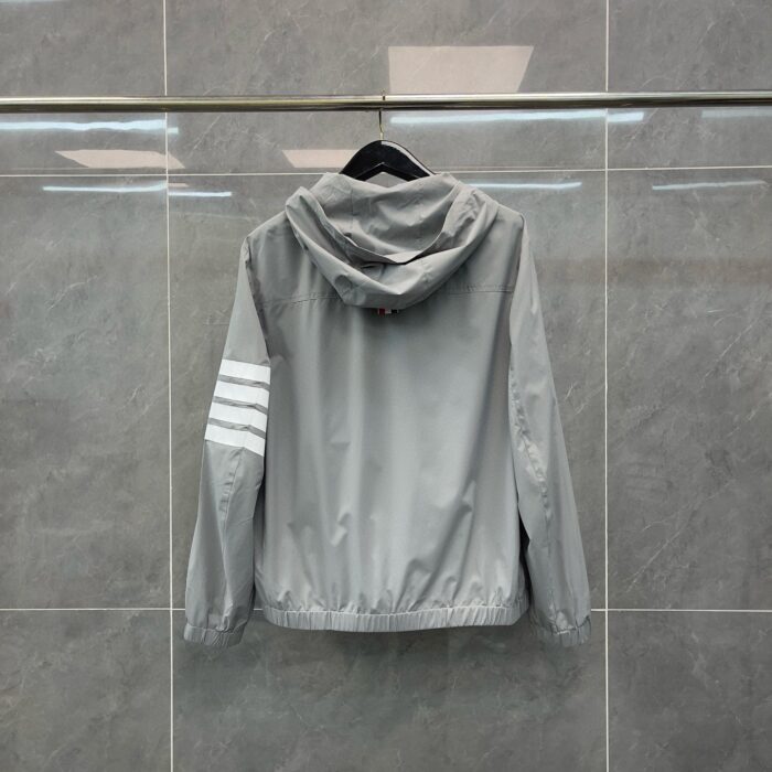 Giacca sportiva grigia con cappuccio e strisce bianche sulla manica, stile casual e moderno.