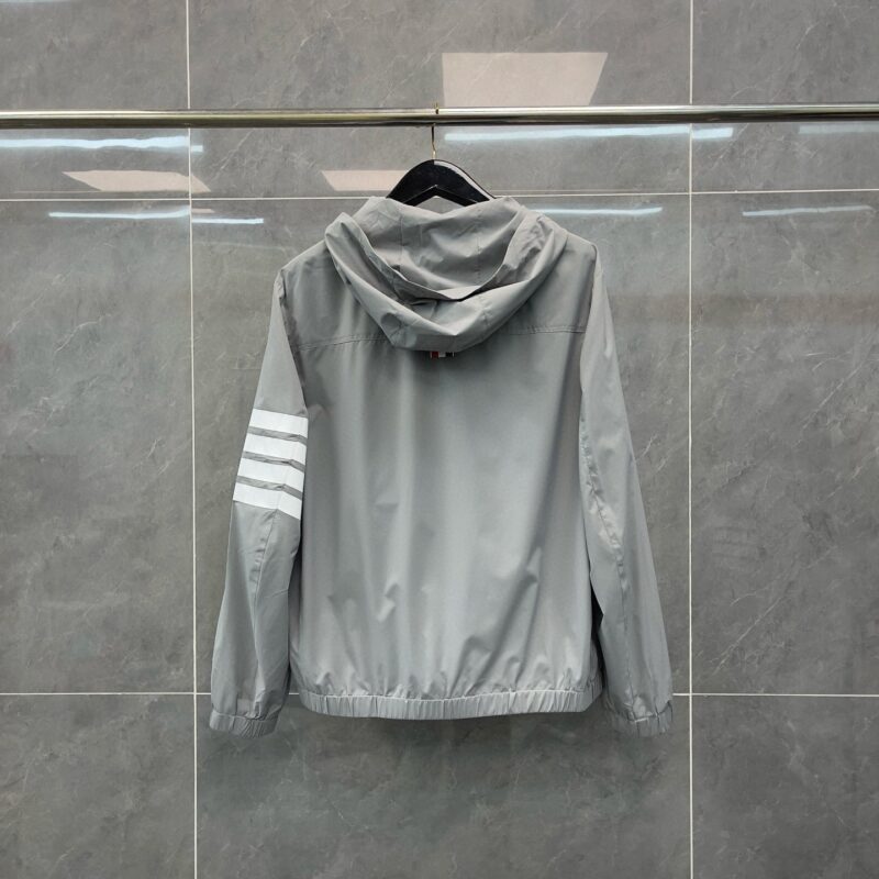 Giacca sportiva grigia con cappuccio e strisce bianche sulla manica, stile casual e moderno.