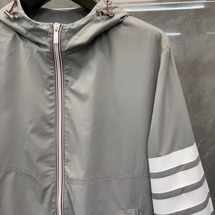 Giacchetto grigio leggero sportivo con cappuccio e dettagli a strisce bianche, versatile e moderno.