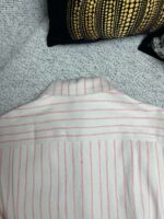 Camicia bianca a righe rosse su sfondo accogliente con cuscino decorativo.
