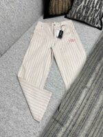 Pantaloni uomo leggeri a righe sottili, eleganti e moderni, su divano grigio con logo ricamato.