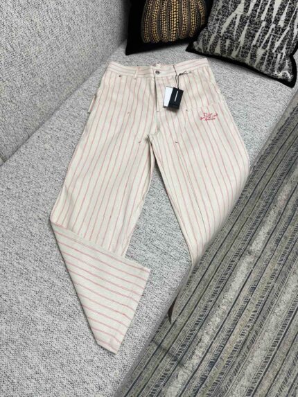 Pantaloni uomo leggeri a righe sottili, eleganti e moderni, su divano grigio con logo ricamato.