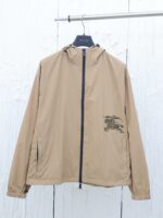 Giacca beige leggera con cappuccio, zip frontale e ricamo verde decorativo.