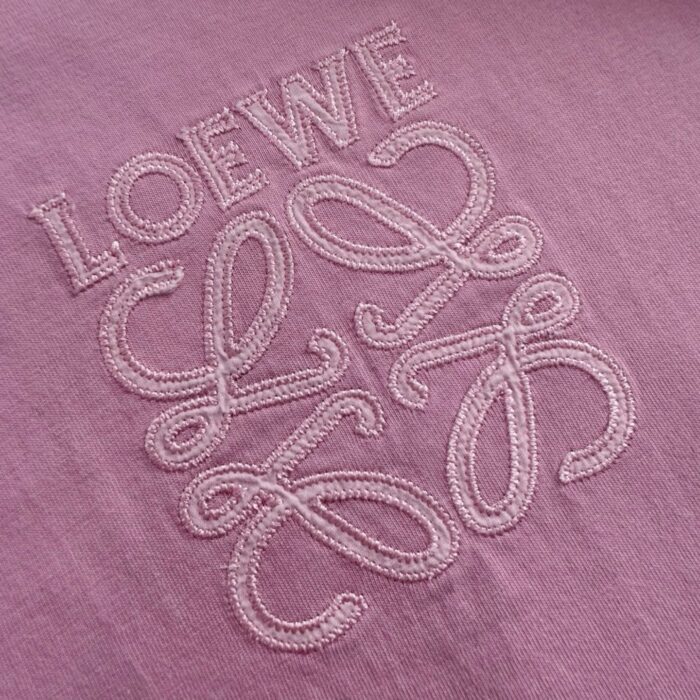Ricamo Loewe su tessuto viola pastello, elegante e di alta qualità.