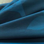Tessuto blu e teal con motivi astratti, effetto lucido e texture morbida.