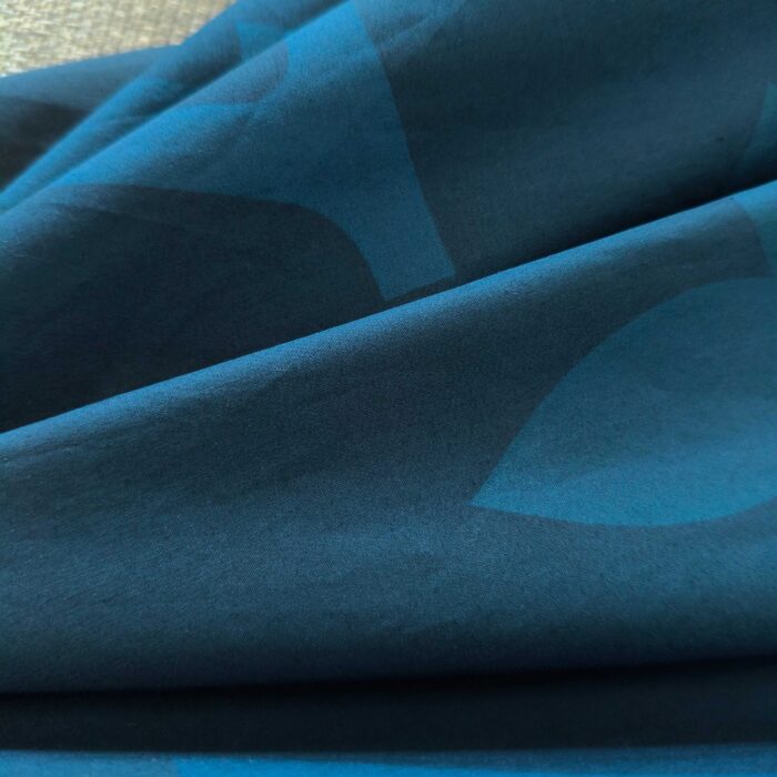 Tessuto blu e teal con motivi astratti, effetto lucido e texture morbida.