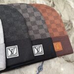 Cappelli beanie di lusso con logo e fantasie in tonalità neutre e calde su base in marmo.