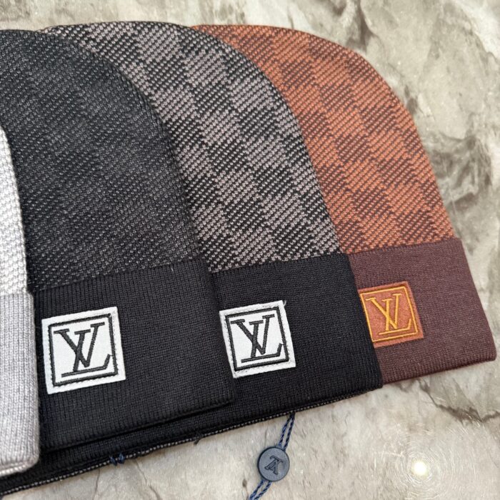 Cappelli beanie di lusso con logo e fantasie in tonalità neutre e calde su base in marmo.