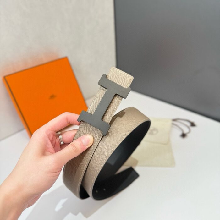 Cintura di lusso beige con fibbia H e stile elegante, inquadratura su mano e confezione colorata.