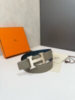 Cintura di lusso con fibbia H in argento, scatola arancione e custodia bianca elegante.