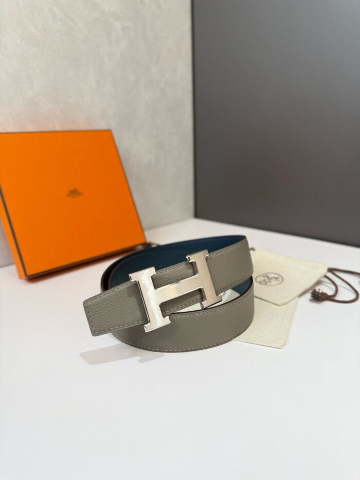 Cintura di lusso con fibbia H in argento, scatola arancione e custodia bianca elegante.