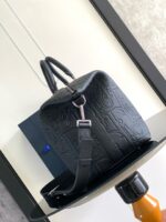 Borsa nera elegante con dettagli embossati e tracolla regolabile, su tavolo lucido moderno.