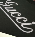 Dettaglio di logo elegante su maglietta nera di lusso, tessuto di alta qualità e stile raffinato.