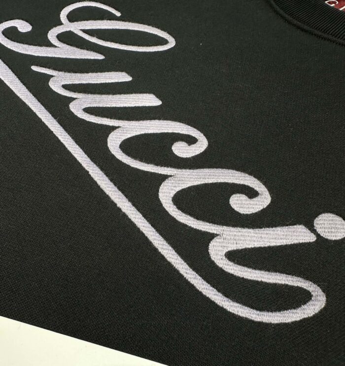 Dettaglio di logo elegante su maglietta nera di lusso, tessuto di alta qualità e stile raffinato.