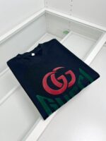 Maglietta nera Gucci con logo colorato e style streetwear su mensola di vetro elegante.