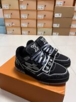 Sneakers nere di lusso con logo elegante, su scatola arancione in ambiente retail moderno.