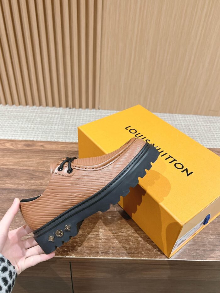 Sneaker di lusso in pelle caramello con suola nera e box giallo brillante, stile elegante.