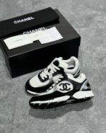Sneakers Chanel di lusso con logo CC, scatola elegante e dettagli raffinati su superficie grigia.