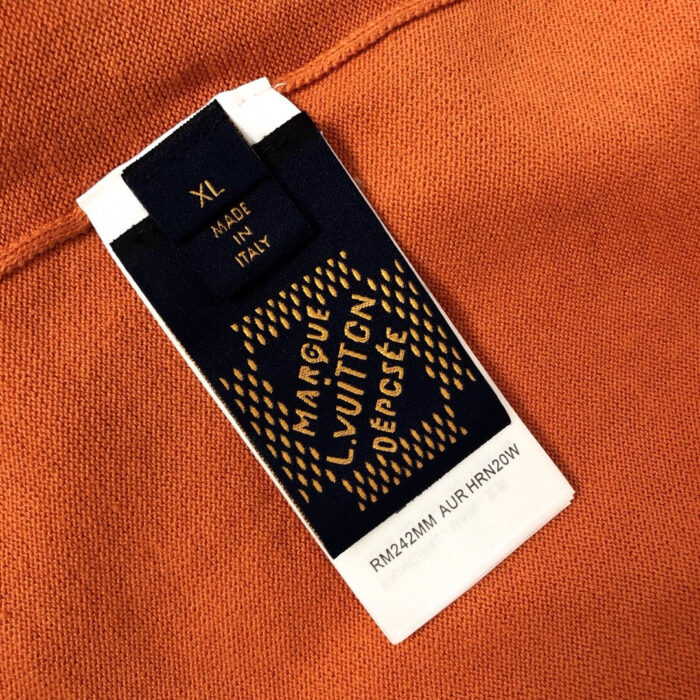 Etichetta di lusso Louis Vuitton su tessuto arancione, con dettagli eleganti e branding esclusivo.