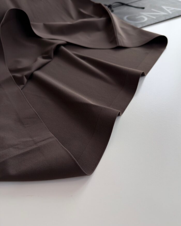Tessuto marrone scuro, lucido e morbido, con drappeggio elegante per moda e decorazione.