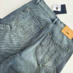 Jeans di lusso in denim chiaro con ricami logo, rivetti oro e patch in pelle.