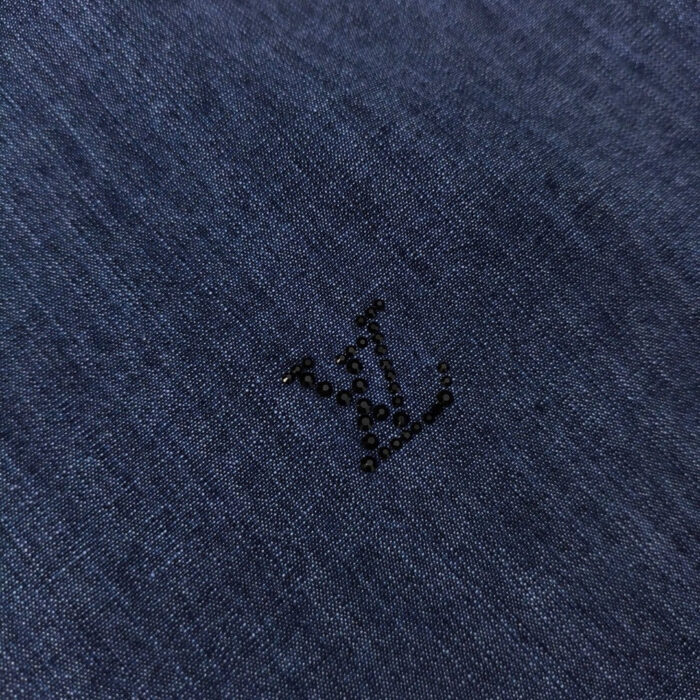 Dettaglio di denim blu con logo minimalista in fibra nera, eleganza moderna e raffinata.