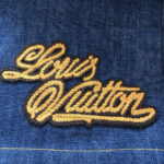Ricamo Louis Vuitton su jeans in denim blu, logo dorato elegante e casual.