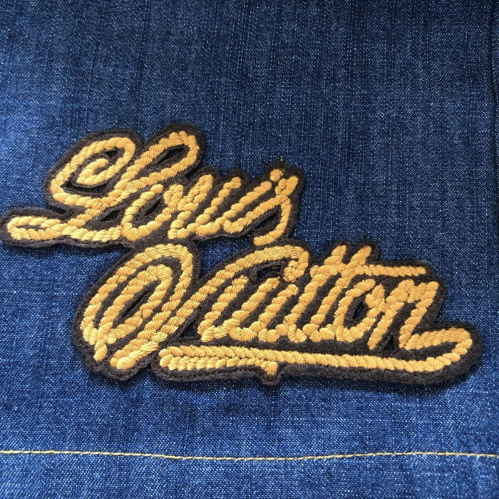 Ricamo Louis Vuitton su jeans in denim blu, logo dorato elegante e casual.