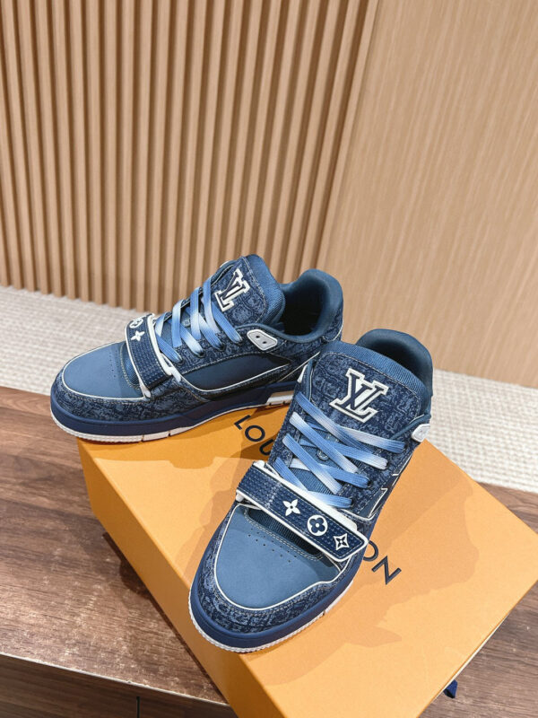 Sneaker da uomo in denim blu, dettagli bianchi e suola pulita su scatola arancione di lusso.