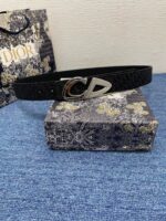 Cintura Dior nera con fibbia CD, packaging elegante e sfondo blu raffinato.
