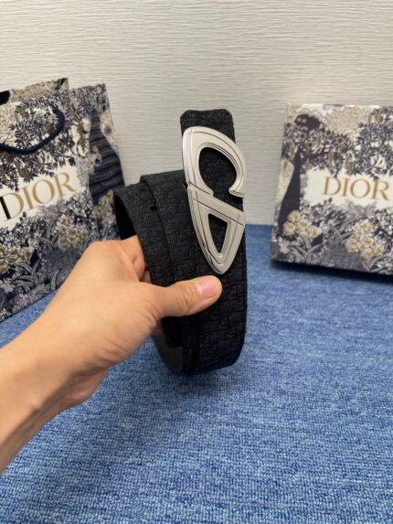 Cintura Dior in tessuto elegante con fibbia moderna, sfondo con borse di lusso e dettagli raffinati.