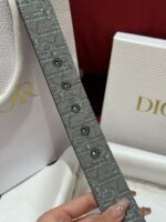 Cintura Dior di lusso con bottoni neri e packaging elegante in crema e oro.