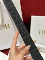 Cintura Dior nera texturizzata con unghie pastel, accessorio di lusso in elegante contesto.