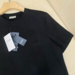 Maglietta Dior nera in cotone di alta qualità, elegante e versatile, su appendiabiti in legno.