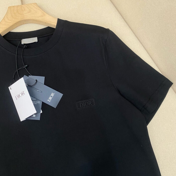 Maglietta Dior nera in cotone di alta qualità, elegante e versatile, su appendiabiti in legno.