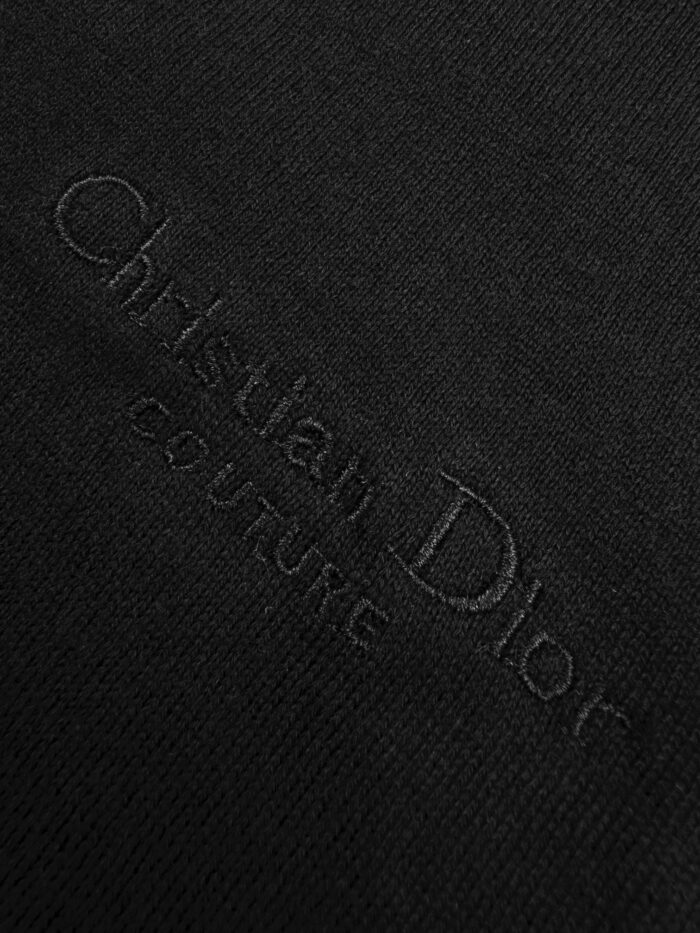 Dettaglio di tessuto nero Dior Couture con logo embossato, simbolo di eleganza e alta moda.