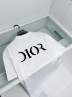 Maglietta Dior bianca in vetrina di lusso con logo nero e design elegante.
