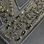 Tessuto nero con ricami metallici e gemme scintillanti, dettaglio decorativo elegante e sofisticato.