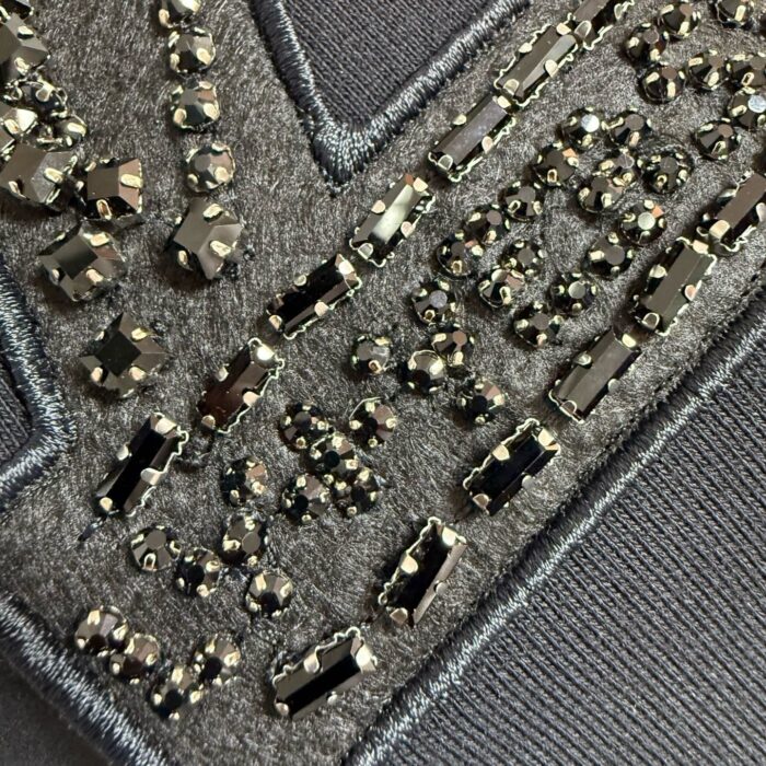 Tessuto nero con ricami metallici e gemme scintillanti, dettaglio decorativo elegante e sofisticato.