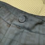 Dettaglio di pantaloni eleganti con tessuto lucido e bottone logato di alta qualità.
