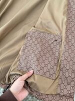 Dettaglio di cappotto di lusso con tasca monogramma Gucci, tessuti eleganti e artigianato raffinato.