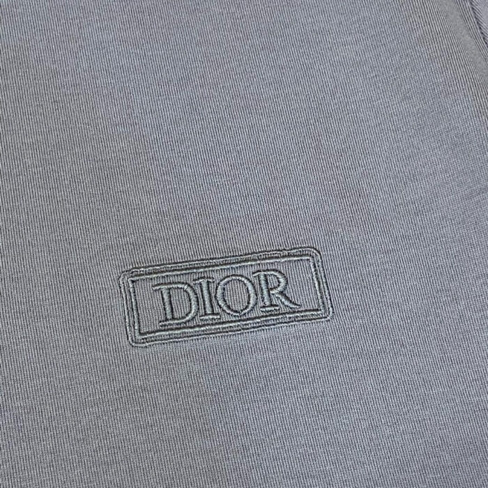Dettaglio di tessuto grigio con logo Dior ricamato, stile minimalista ed elegante.