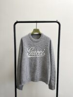 Maglione grigio Gucci con ricamo del logo, stile casual e di lusso, display minimalista.